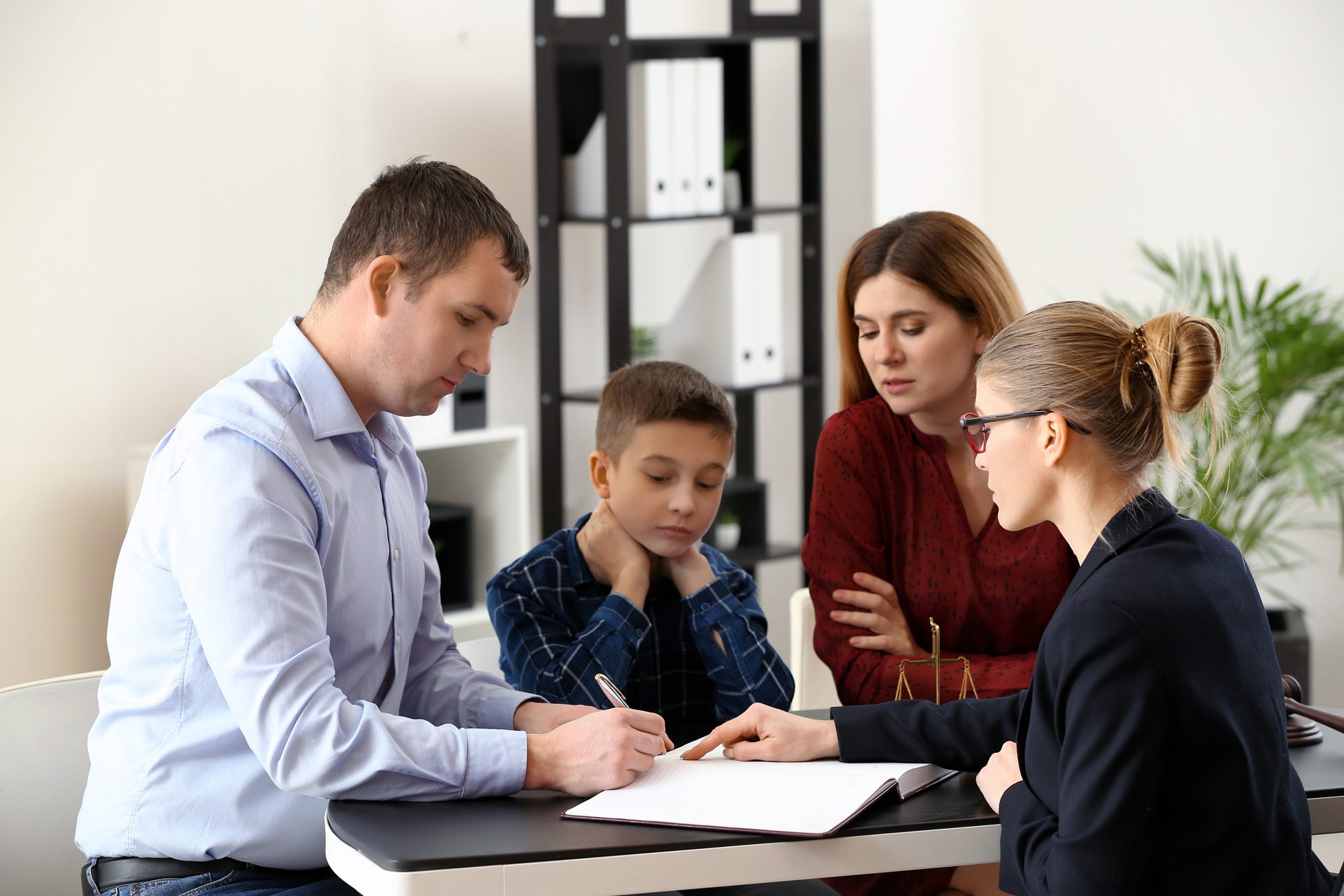 A divorced couple, with their son, settle their custody case, as the father’s child custody attorney at Clearwater Law Group has him sign the custody agreement.